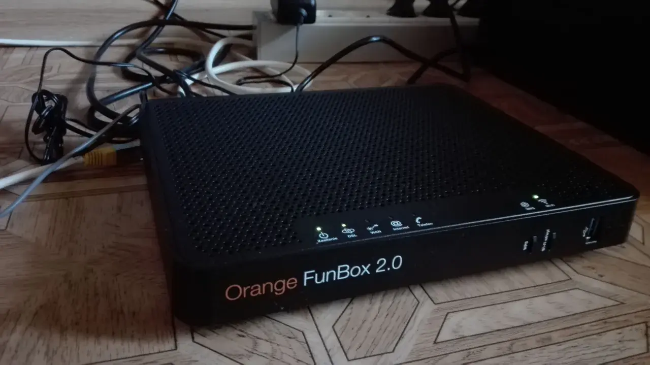 Czarny router Orange FunBox 2.0 z wieloma kablami podłączonymi do listwy zasilającej.