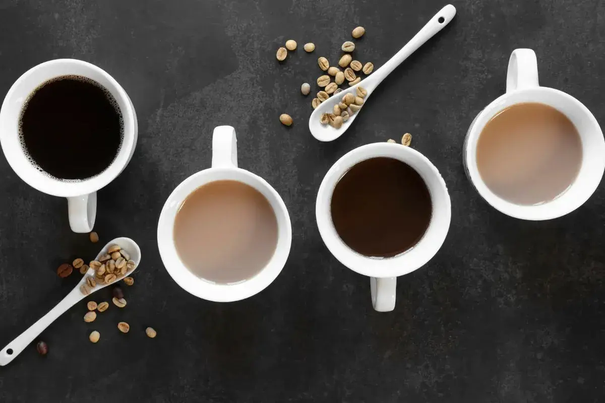 Vier Tassen Kaffee, zwei schwarz, zwei mit Milch, und Löffel mit Kaffeebohnen. Ein gemütlicher Tee-Teein-Moment.