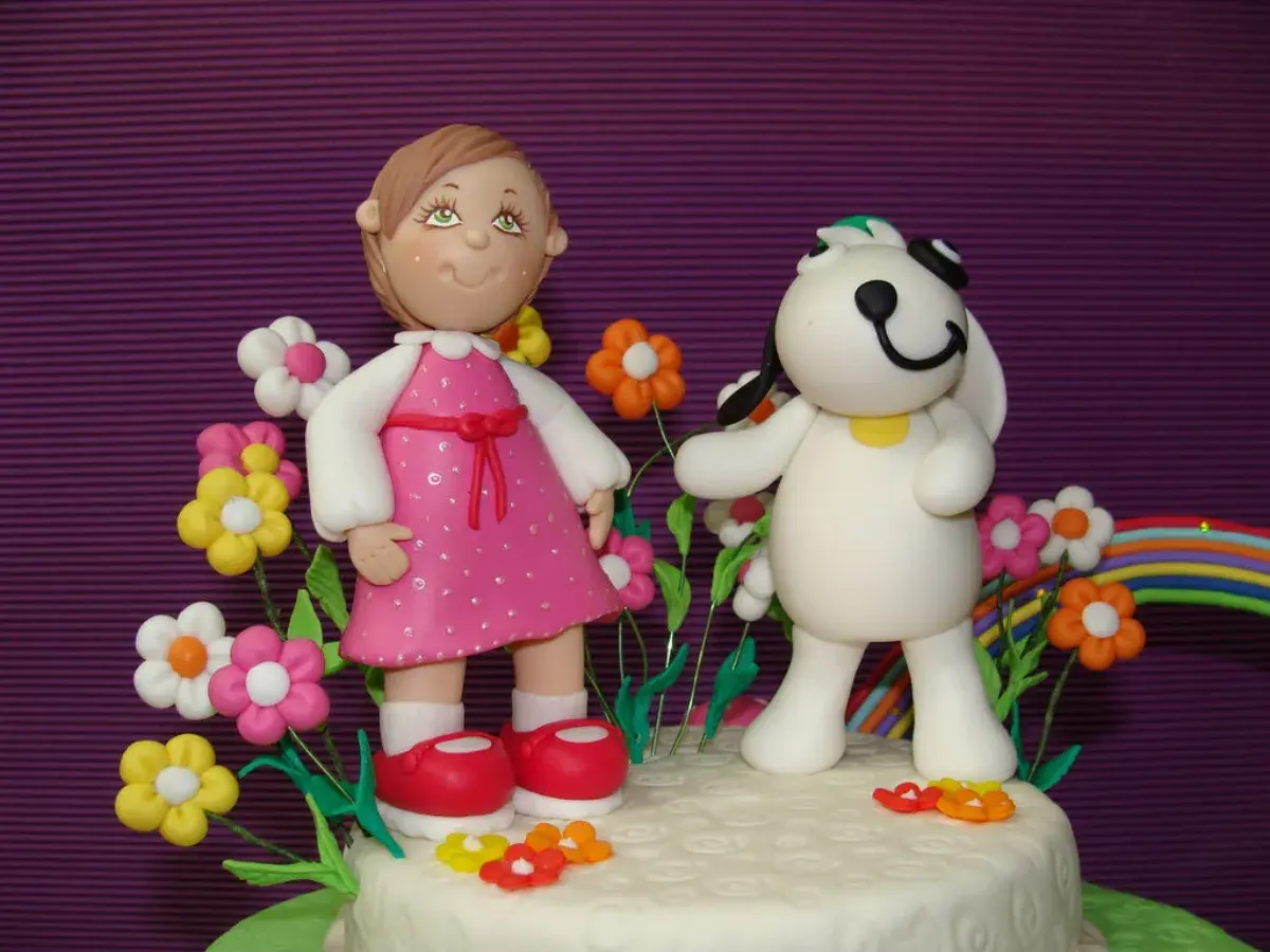 Figuras de porcelana fría: niña con vestido rosa y perro blanco rodeados de flores y un arcoíris.