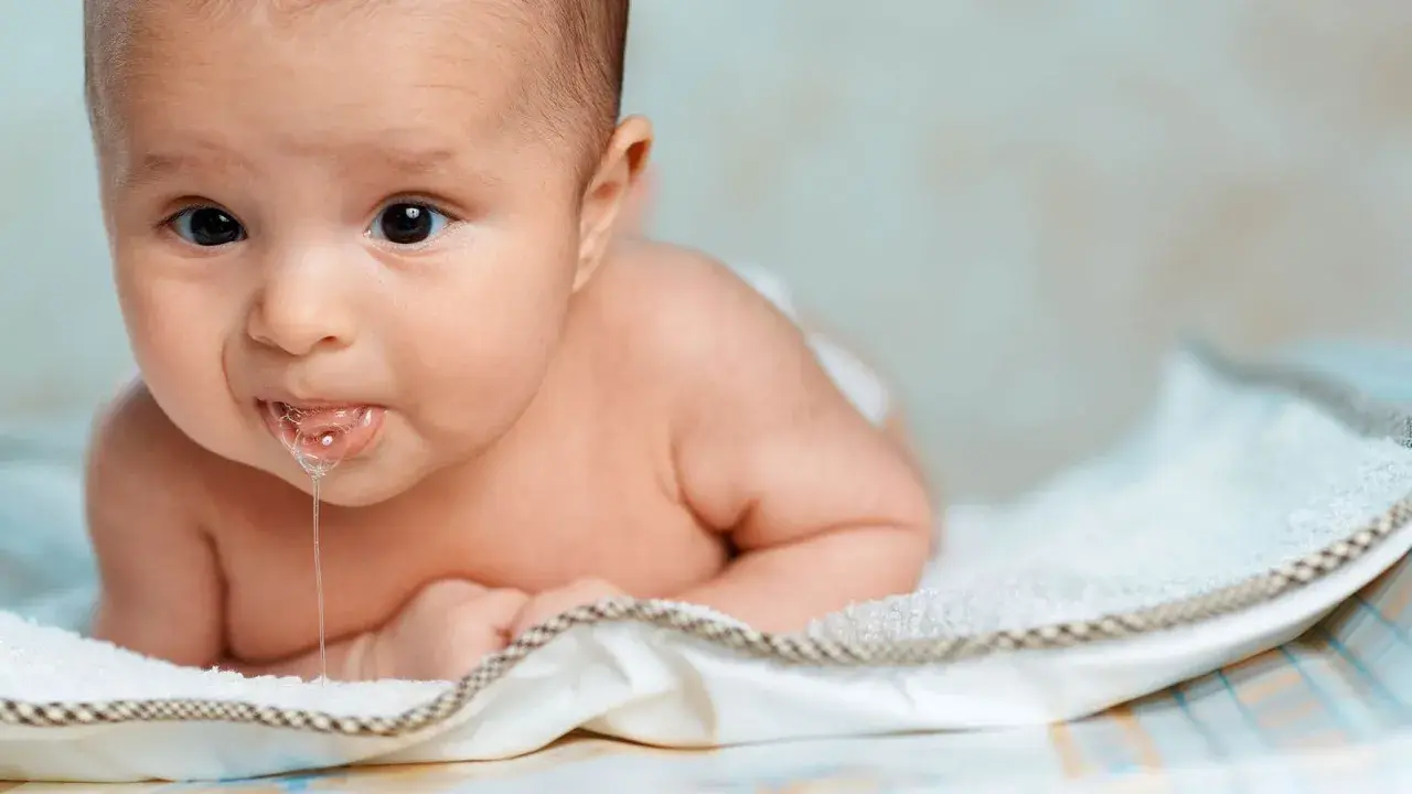 En bebis ligger på mage och det rinner saliv ur munnen. Bebis spyr mycket och det syns bubblor.