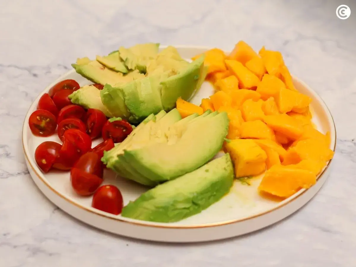 Plato con ensalada de mango y aguacate, tomates cherry cortados por la mitad y aguacate en láminas.
