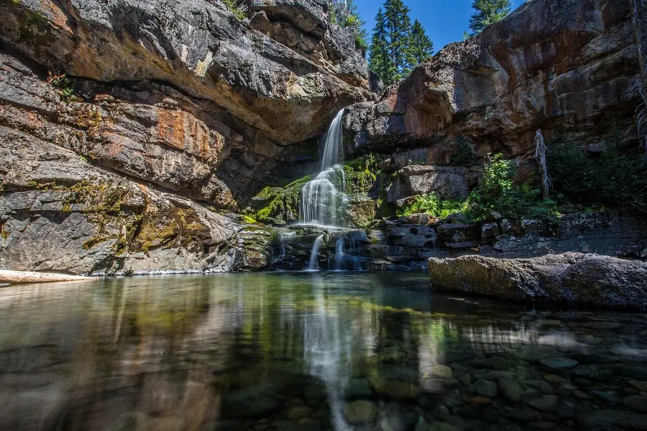 Cascadas en León, agua cristalina cae sobre rocas cubiertas de musgo, reflejándose en un estanque sereno.