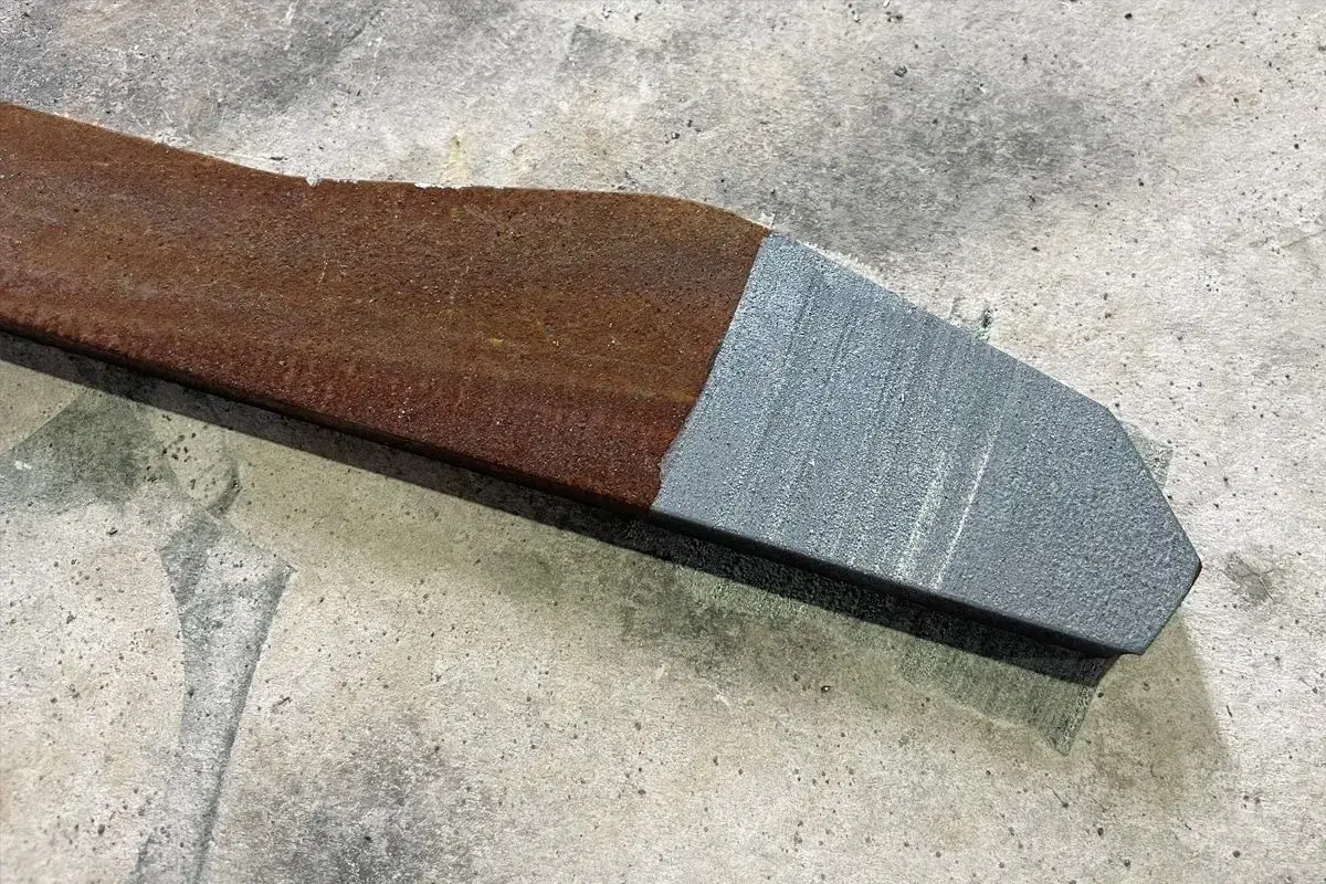 Fragment metalu po jednej stronie zardzewiały, po drugiej idealnie czysty dzięki czyszczeniu laserowemu.