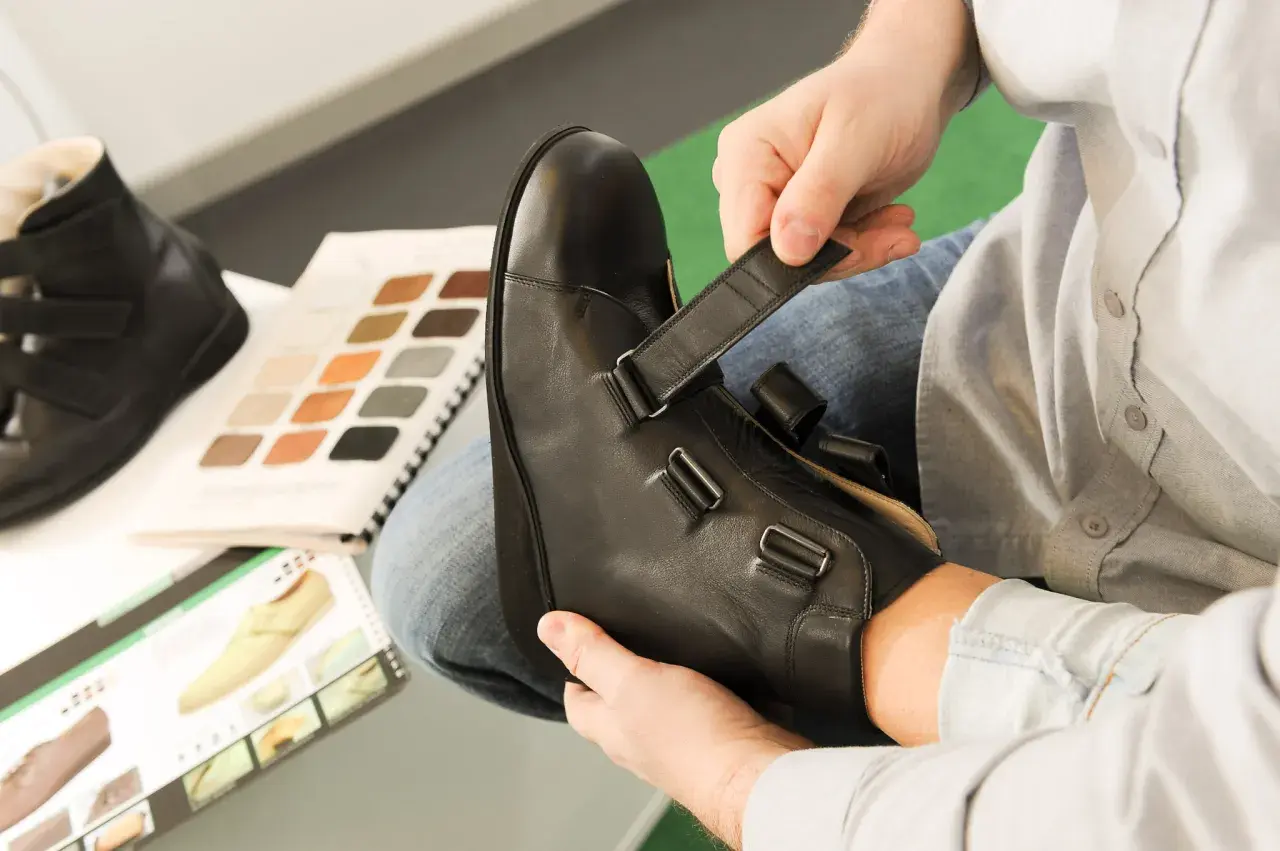 Mann passt orthopädische Schuhe an. Materialmuster und Schuhkatalog liegen bereit. Die orthopädische schuhe kosten sind hier ein wichtiges Thema.