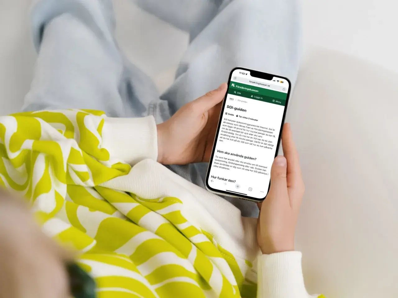 Person håller upp en mobiltelefon som visar Försäkringskassans SGI-guide. Guiden förklarar vad SGI är och hur den fungerar för enskild firma.