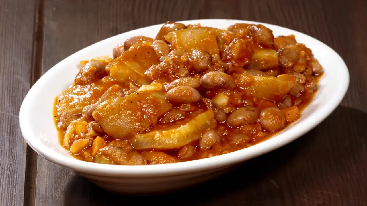 Piatto fumante di fagioli con le cotiche, un classico della ricetta marchigiana, servito in una ciotola bianca su un tavolo di legno scuro.