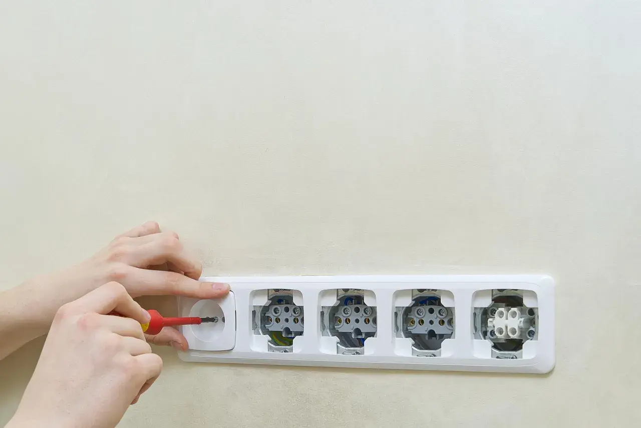 Montaż gniazdek elektrycznych. Ręce przykręcają śrubokrętem jedno z gniazdek w listwie. Schemat instalacji elektrycznej.