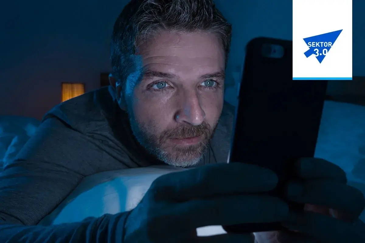 Mężczyzna wpatruje się w ekran telefonu w ciemności, jego oczy błyszczą. Czy to uzależnienie od muzyki, czy od mediów społecznościowych?