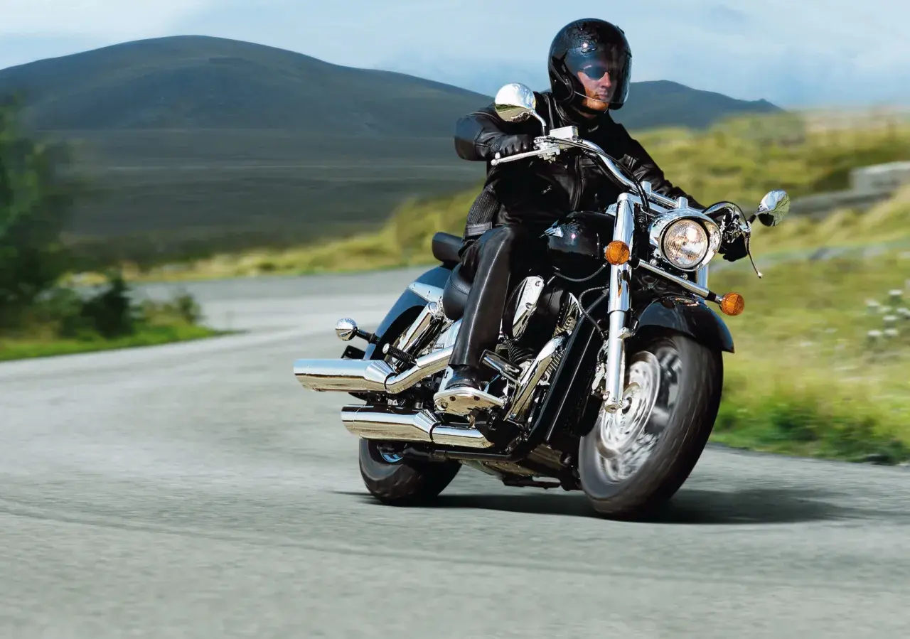 Mężczyzna w kasku i skórzanej kurtce jedzie na motocyklu Honda VTX 1800. Wady i zalety tego potężnego cruisera są dyskutowane podczas jazdy po malowniczej drodze.