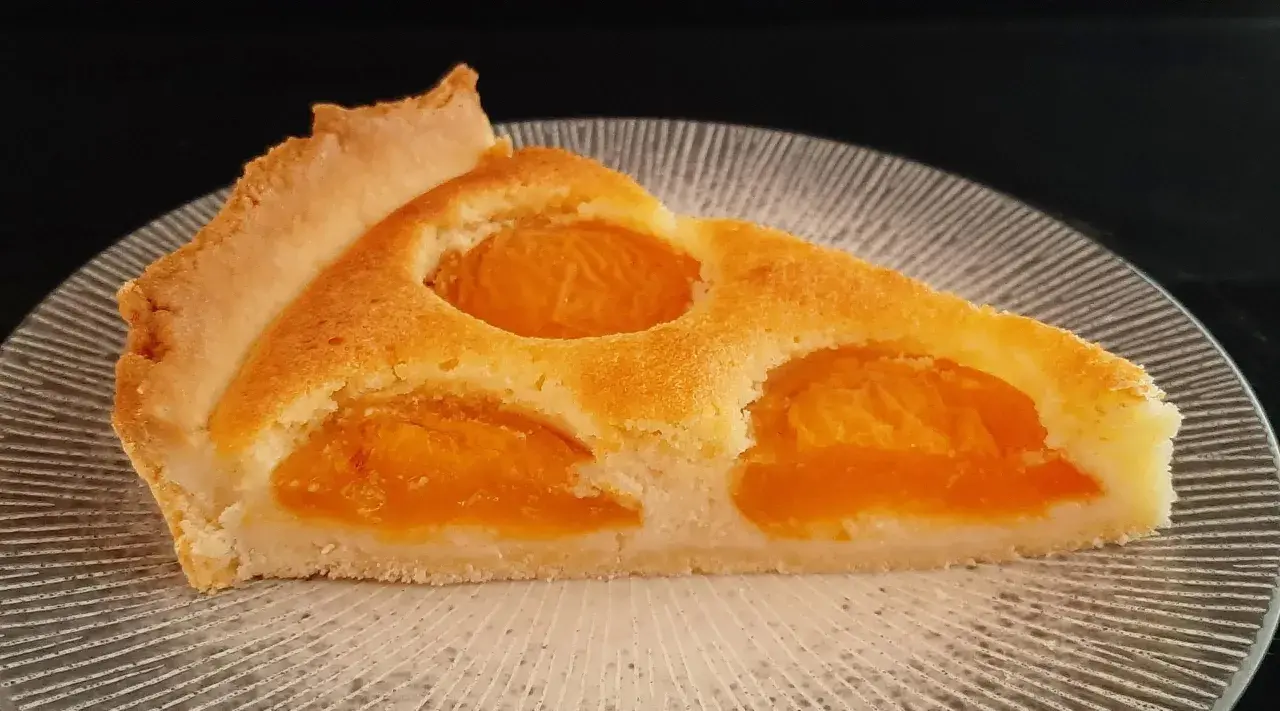 Tranche de tarte aux abricots classique, avec sa pâte dorée et ses fruits juteux, prête à être dégustée.