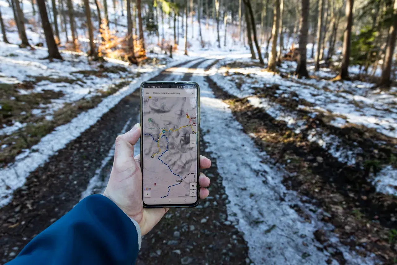 Telefon z mapą pokazuje skopiec trasę w zimowym lesie.