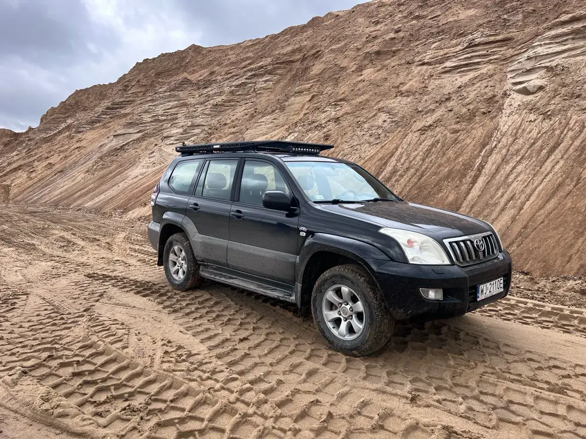 Czarny Land Cruiser 120 na piaszczystym podłożu, z bagażnikiem dachowym, gotowy na terenową przygodę.
