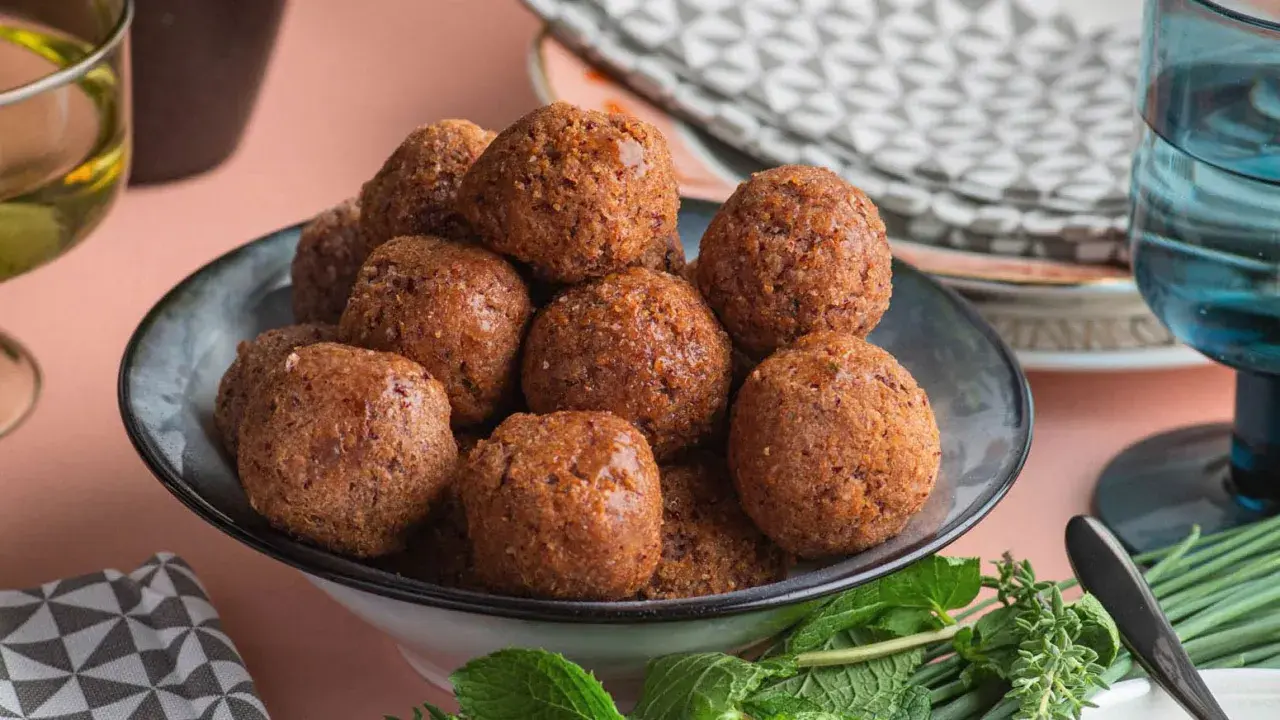 Un piatto pieno di polpette di fagioli dorate, guarnite con erbe fresche.