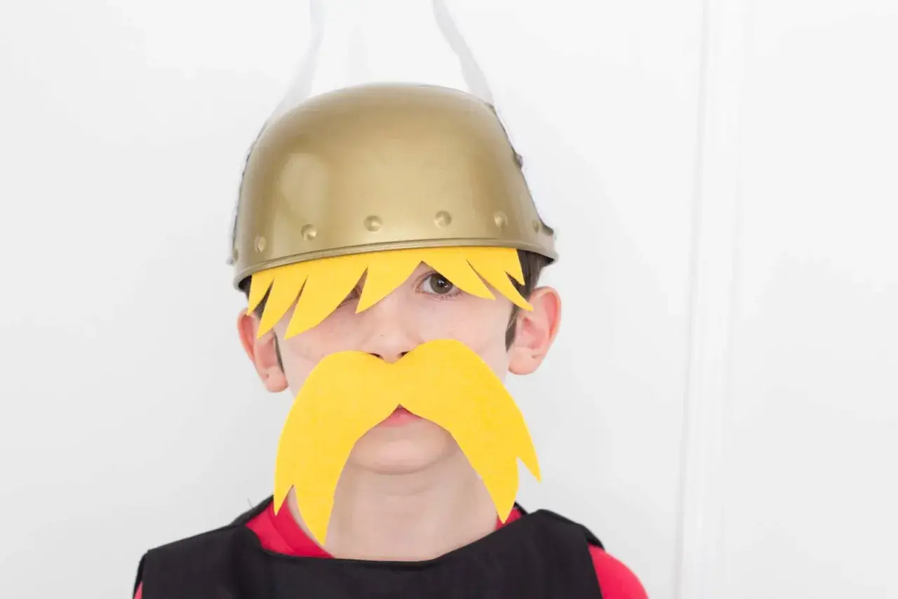 Niño con disfraz casero de Astérix y Obélix, luciendo casco dorado y bigote amarillo.