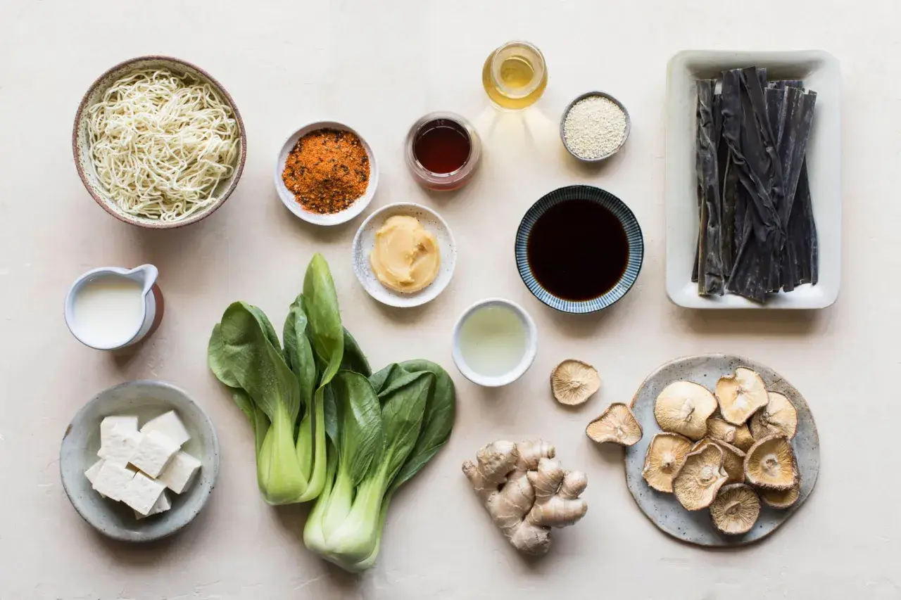 A collection of ingredients for a Japanese meal, including noodles, bok choy, tofu, ginger, dried mushrooms, and various Japanese sauces and seasonings.