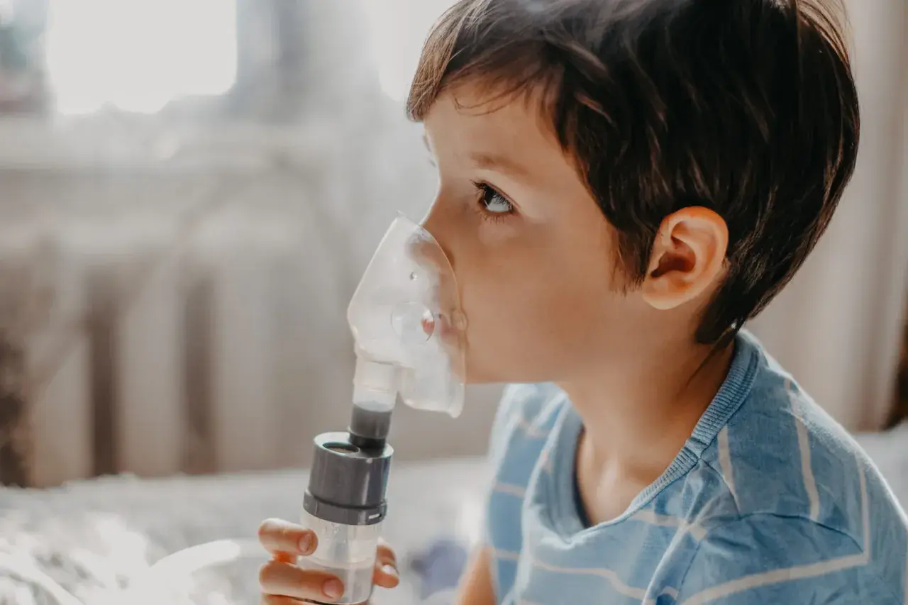 Chłopiec z maską inhalatora na twarzy, wdycha sól fizjologiczną do inhalacji.