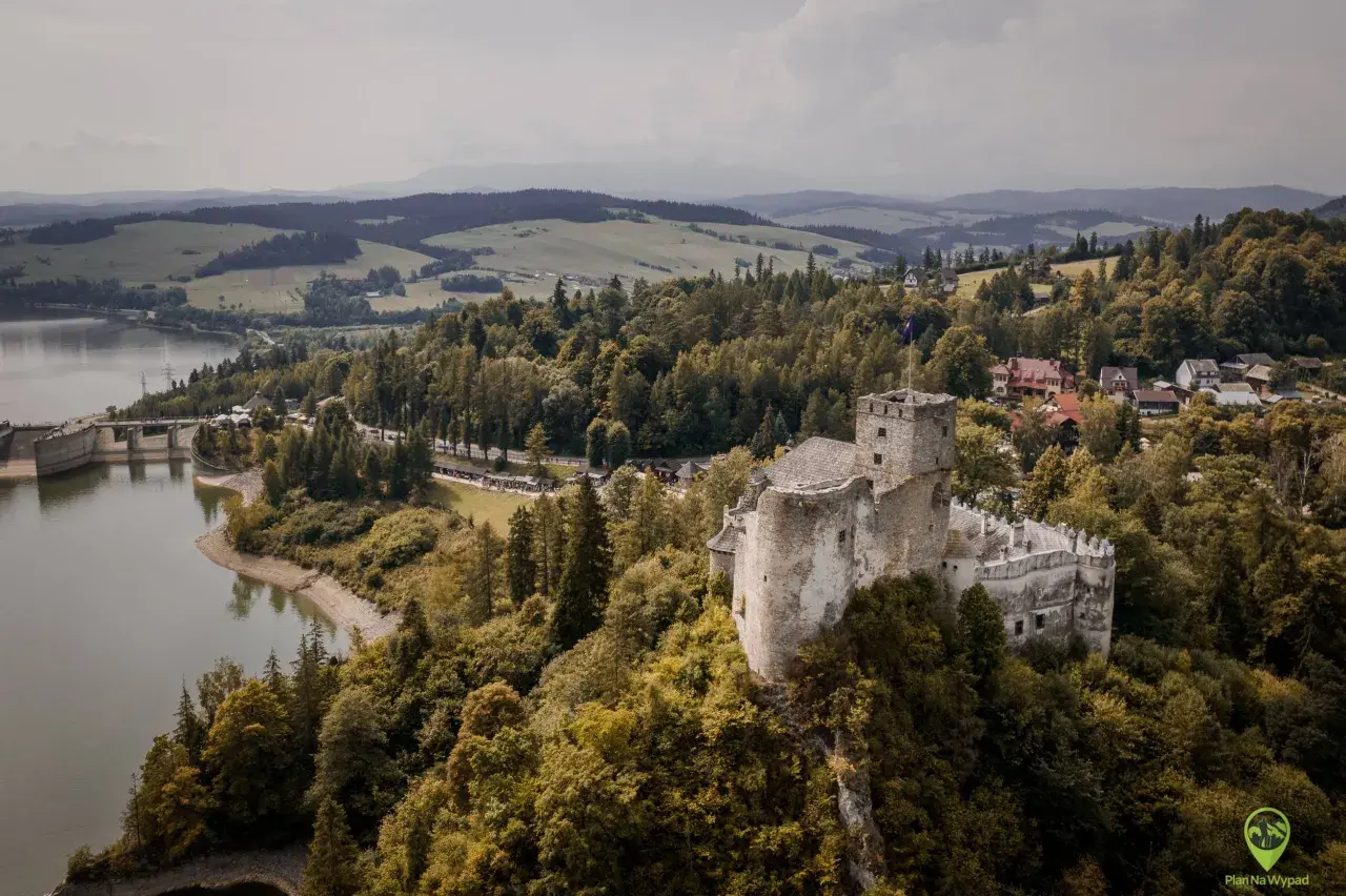 Zamek w Niedzicy góruje nad jeziorem i lasami. W oddali widać góry.