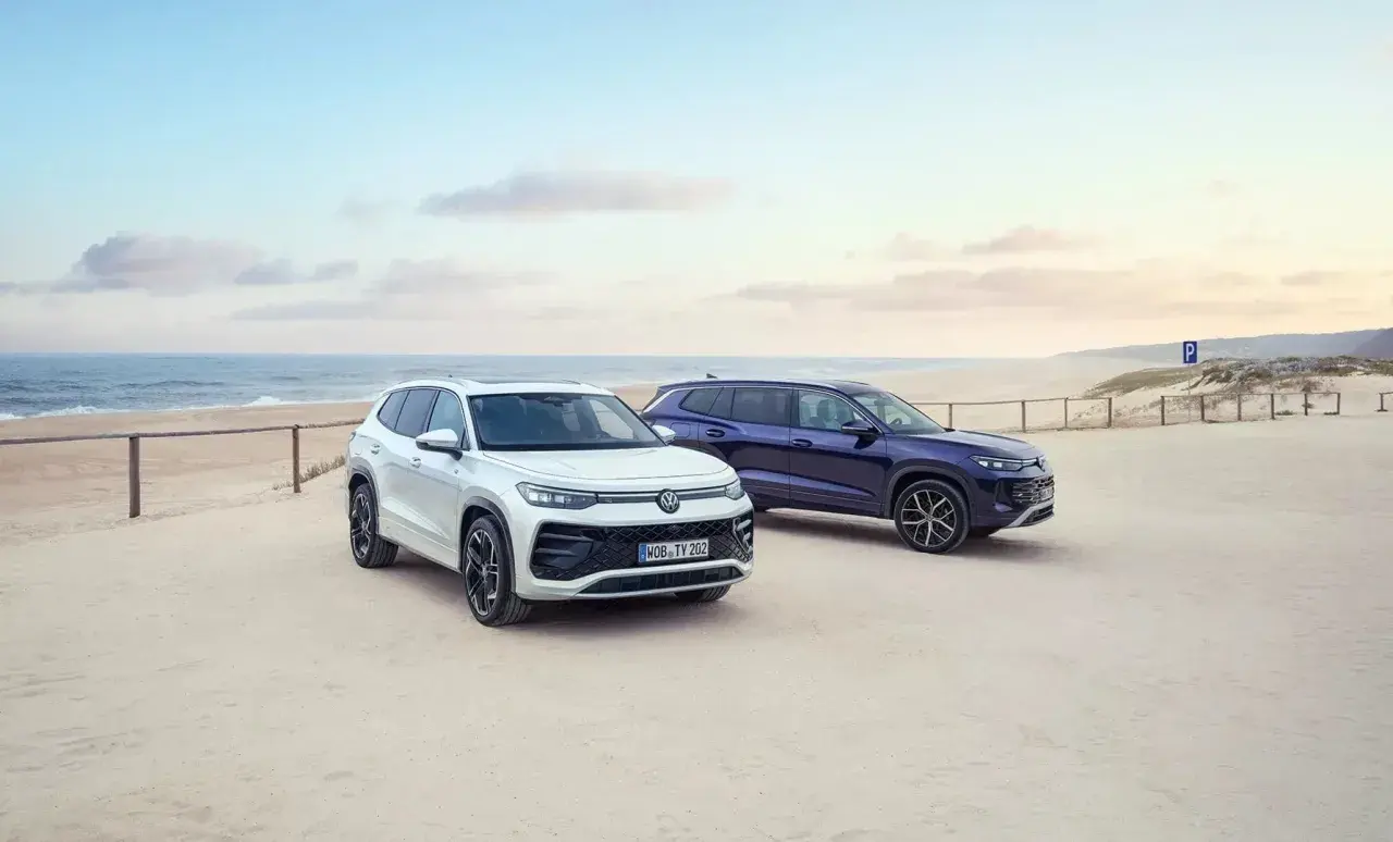 Dwa SUV-y, biały i granatowy, zaparkowane na piaszczystej plaży. To nowe modele VW Tayron, gotowe na przygodę nad morzem.