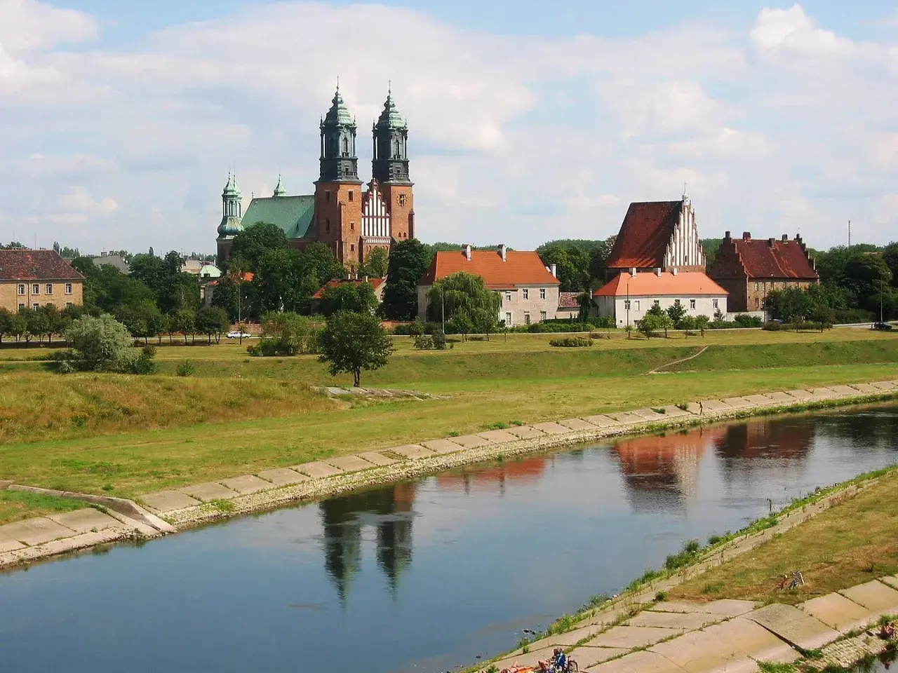 Widok na Ostrów Tumski w Poznaniu z katedrą i innymi zabytkowymi budynkami nad rzeką Wartą.