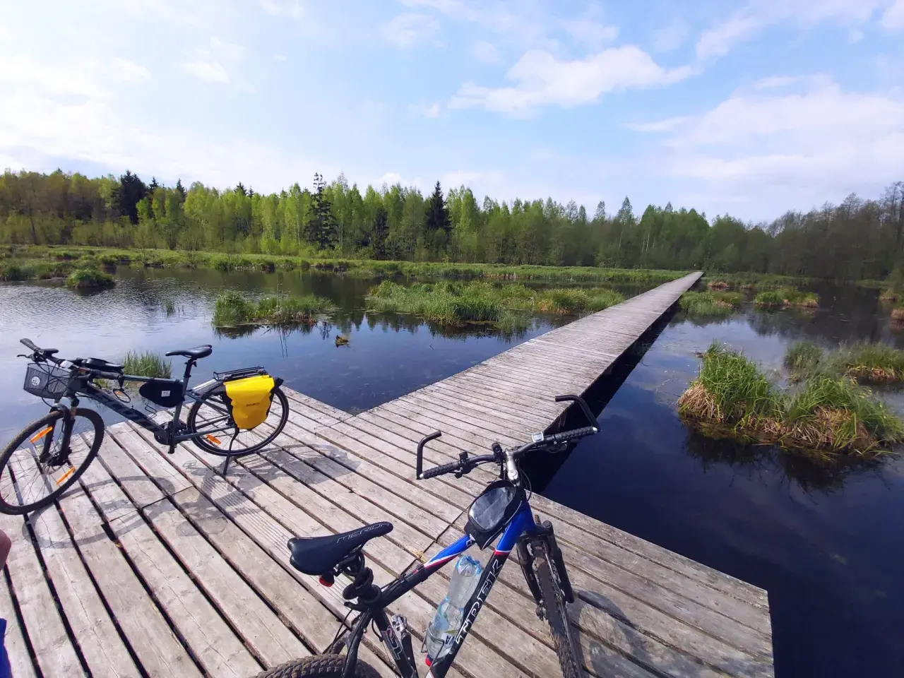 Dwa rowery na drewnianym pomoście nad wodą, otoczone zielenią. Idealne miejsce na odkrywanie tras rowerowych Białystok.