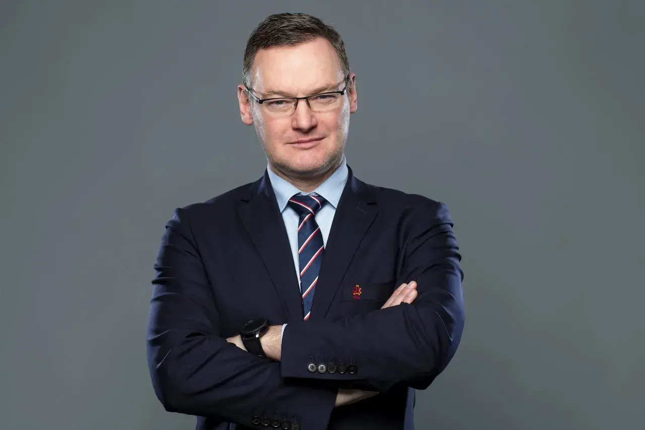 Miłosz Stępiński w granatowym garniturze, z rękami skrzyżowanymi na piersi, patrzy pewnie w obiektyw.