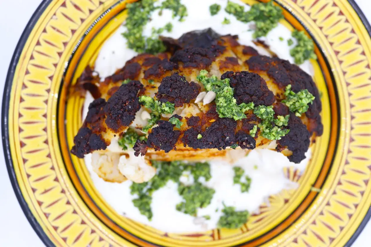 Un chou-fleur rôti, bien caramélisé, servi sur une sauce blanche crémeuse et garni d'une sauce verte et de graines.