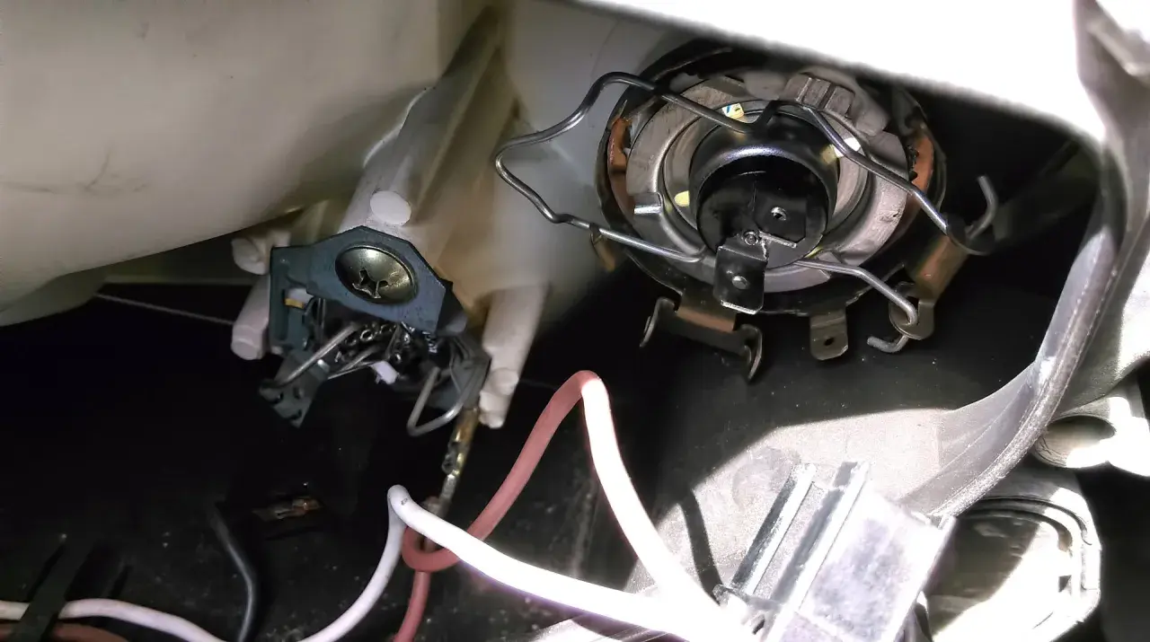 Wymiana żarówki przód Mitsubishi Colt. Widoczny mechanizm mocowania żarówki i przewody.