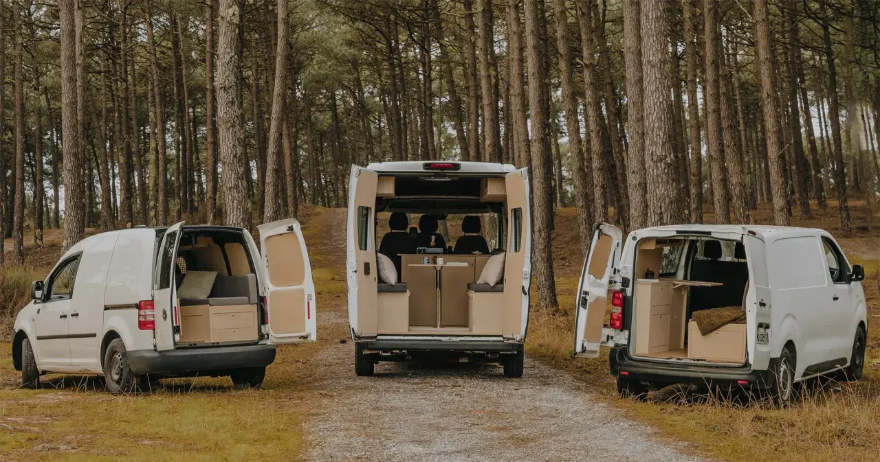 Trois camping-cars aménagés, dont un dimension camping-car 4 places, garés dans une forêt.