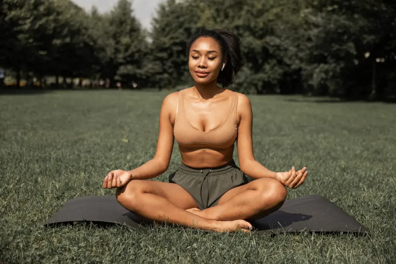 Femme méditant en plein air, une posture de yoga pour maigrir. Elle est assise sur un tapis dans l'herbe, les yeux fermés, en pleine concentration.