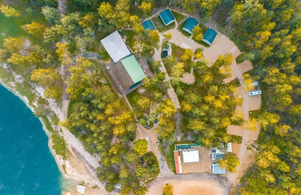 Malowniczy camping w Małopolsce nad turkusową wodą. Domyki, budynki i samochody wśród jesiennych drzew.