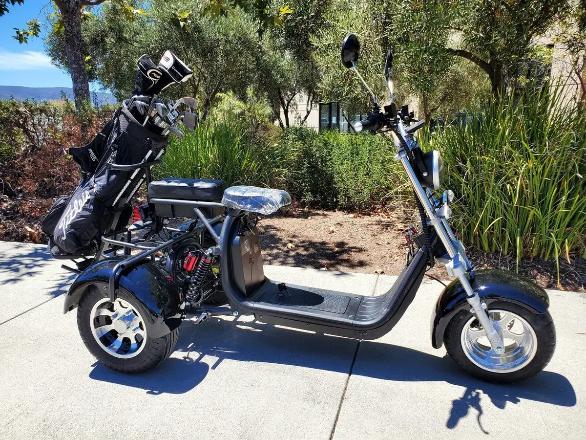 Trike negro de 3 ruedas con bolsa de golf en la parte trasera, aparcado en una acera.