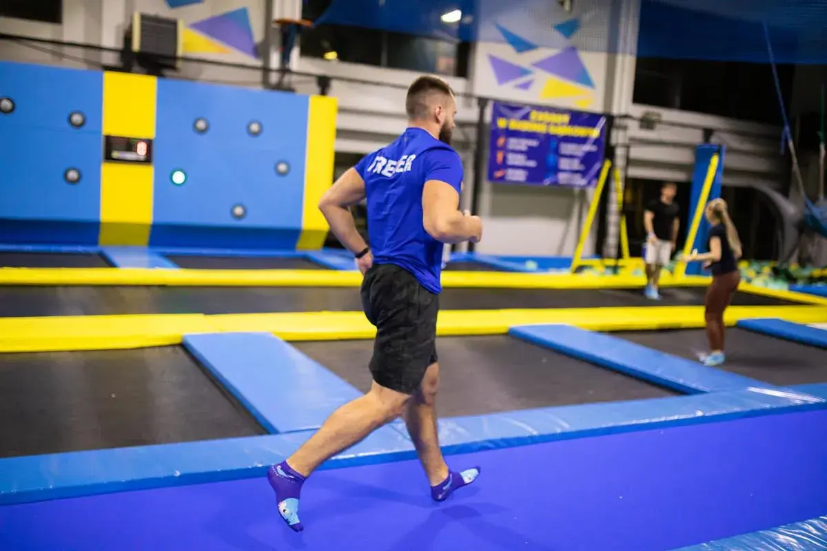Mężczyzna w niebieskiej koszulce wykonuje trening interwałowy na trampolinach.