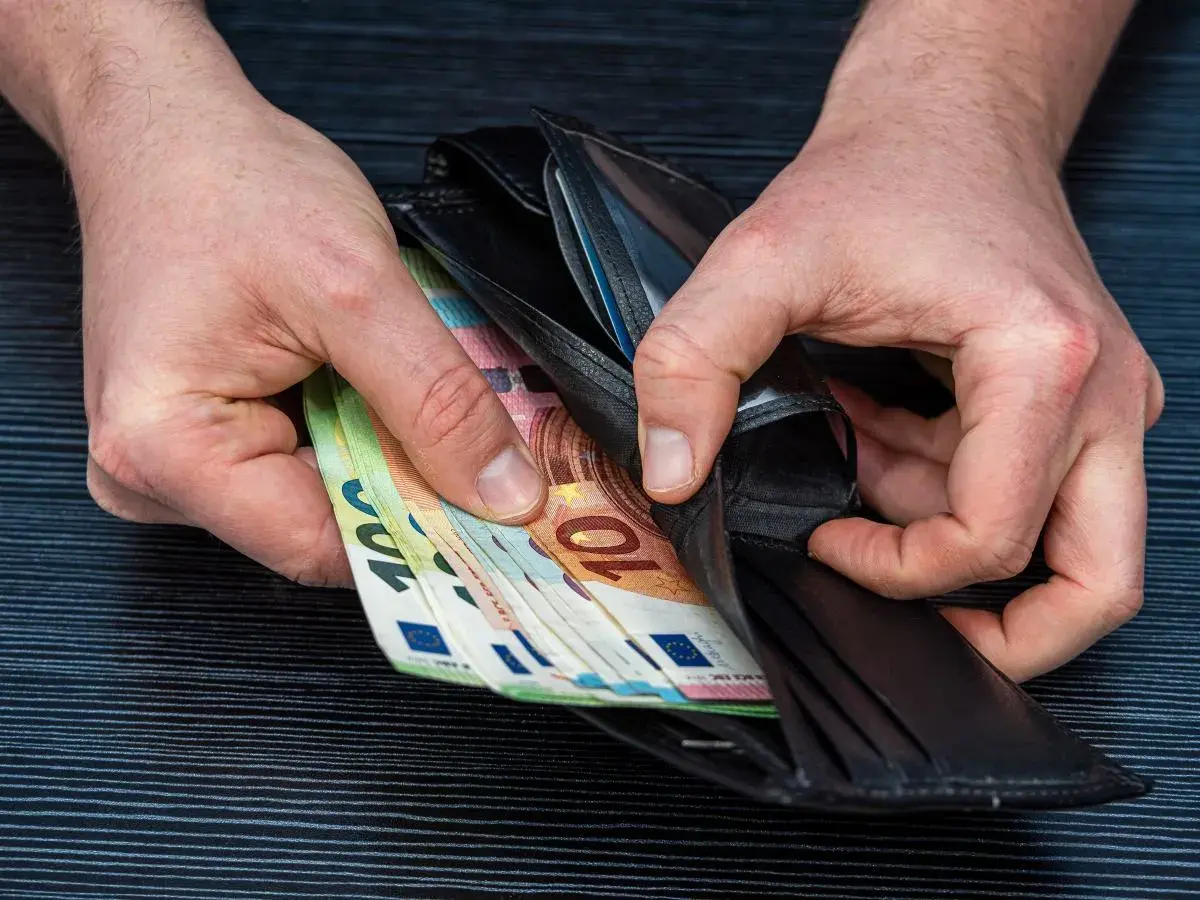 Ręce wkładają do portfela banknoty euro. Zarobione pieniądze po ciężkiej pracy lakiernika.