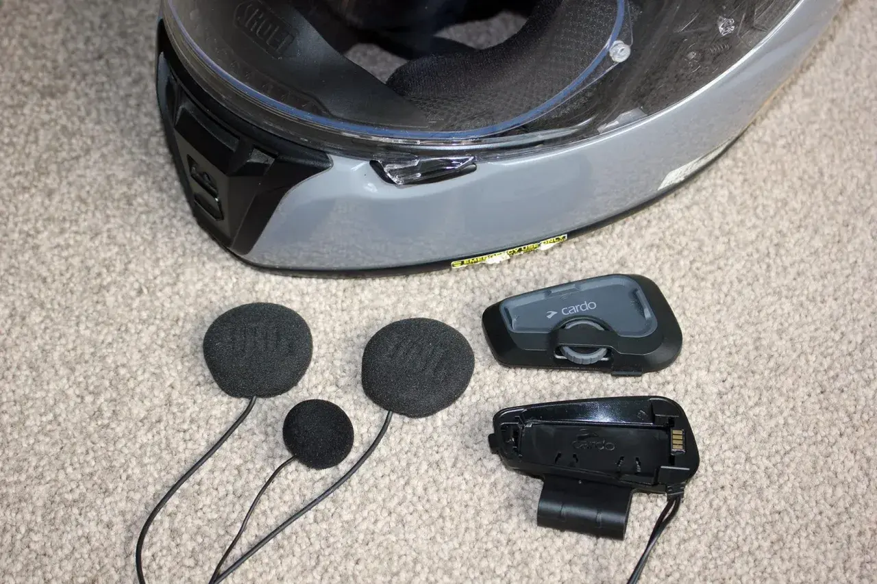 Akcesoria do interkomu motocyklowego Cardo i słuchawki JBL leżą obok kasku. Dowiedz się, jak zamontować interkom do kasku.