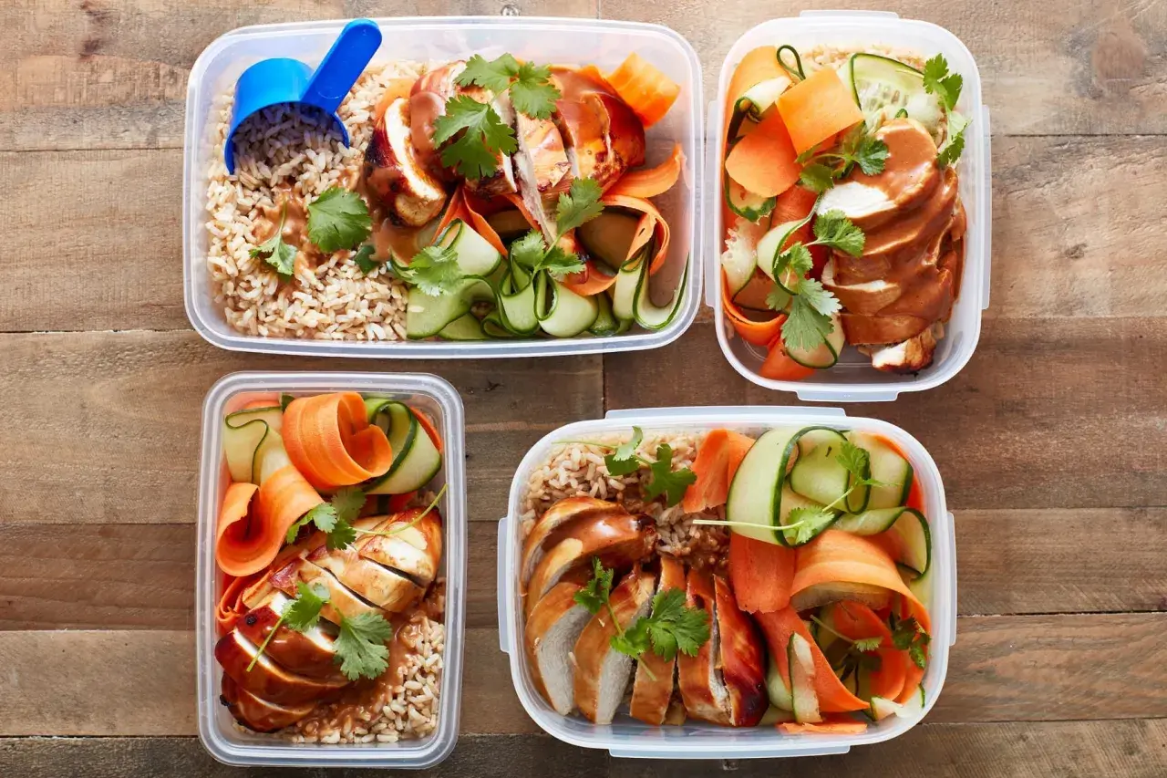 Vier Behälter mit Reis, Hähnchenbrust, Gurken- und Karottenstreifen – perfekt als pre workout meal für Energie.
