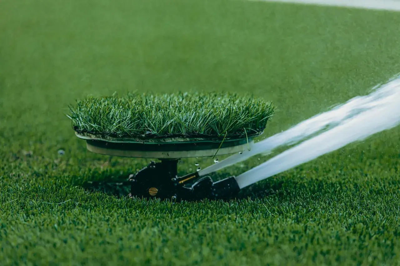 Automatyczne podlewanie trawnika na boisku sportowym. Zraszacze równomiernie rozprowadzają wodę po zielonej murawie.