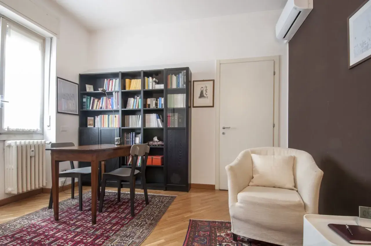 Arredamento accogliente per uno studio di psicoterapia: poltrona comoda, libreria piena e un tavolo per le sedute.