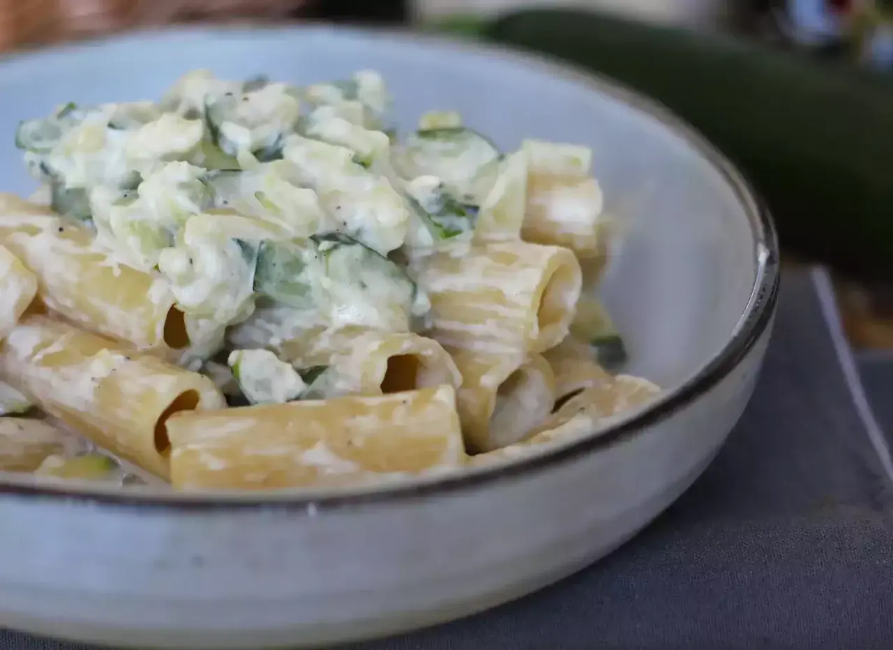 Pasta con calabacín cremosa, servida en un cuenco. Los trozos de calabacín se mezclan con la pasta y una salsa blanca.