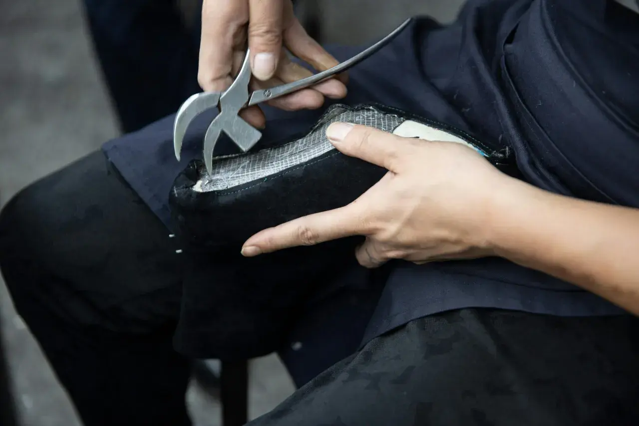Un artisan utilise un outil pour travailler sur un objet en simili cuir noir. La question "peut on peindre du simili cuir" se pose face à cette métamorphose.