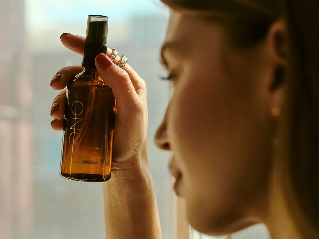 Kobieta trzyma buteleczkę z mgiełką, która zawiera alkohol cetylowy. Delikatna pielęgnacja dla skóry.