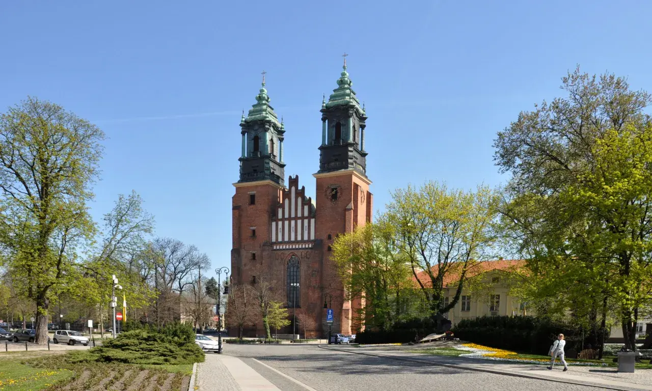 Imponująca katedra w Poznaniu z dwiema wieżami i zielonymi dachami, otoczona drzewami i budynkami.