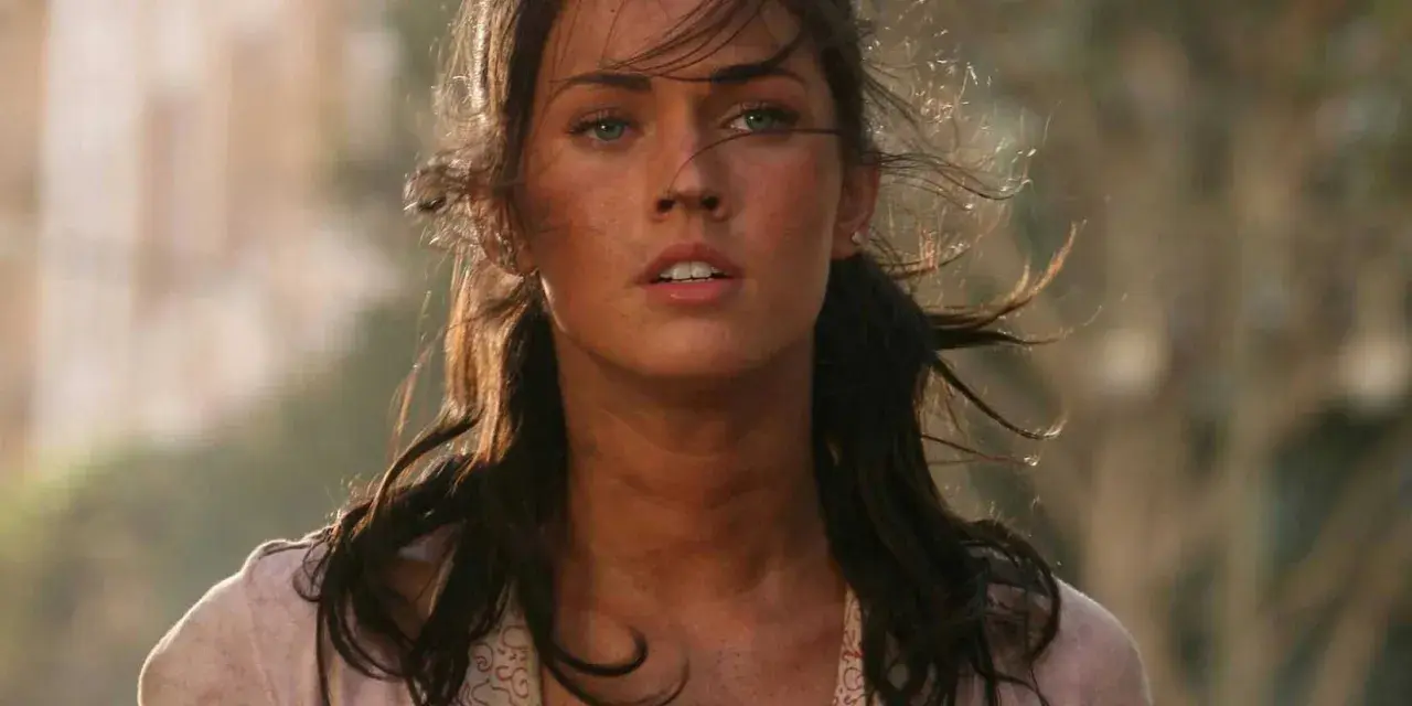 Megan Fox i en dramatisk scen från en av hennes filmer. Hennes hår blåser i vinden och hon ser ut att vara mitt i en actionfylld sekvens.
