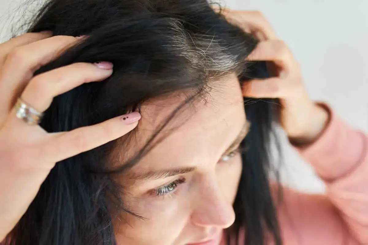 Mani che toccano capelli scuri con ciocche bianche, un segno di come cambiano i capelli nel tempo.