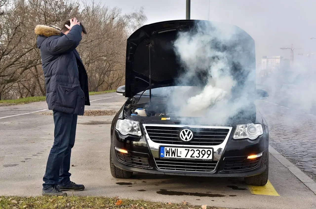 Mężczyzna zrezygnowany patrzy na dym spod maski i czuje zapach spalenizny. Awaria Volkswagena na poboczu.