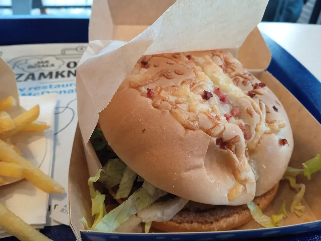Pyszny lumberjack burger z McDonald's w papierowym opakowaniu, obok złociste frytki.
