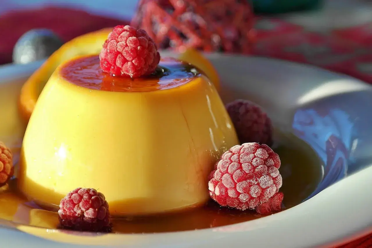 Crème aux œufs onctueuse, nappée de caramel et garnie de framboises givrées. Un délice visuel et gustatif.
