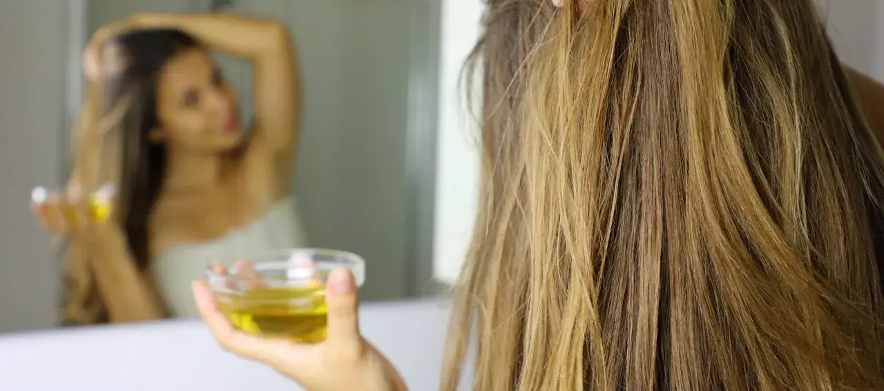 Mujer se aplica aceite de oliva en el cabello, demostrando que el aceite de oliva es bueno para el pelo.