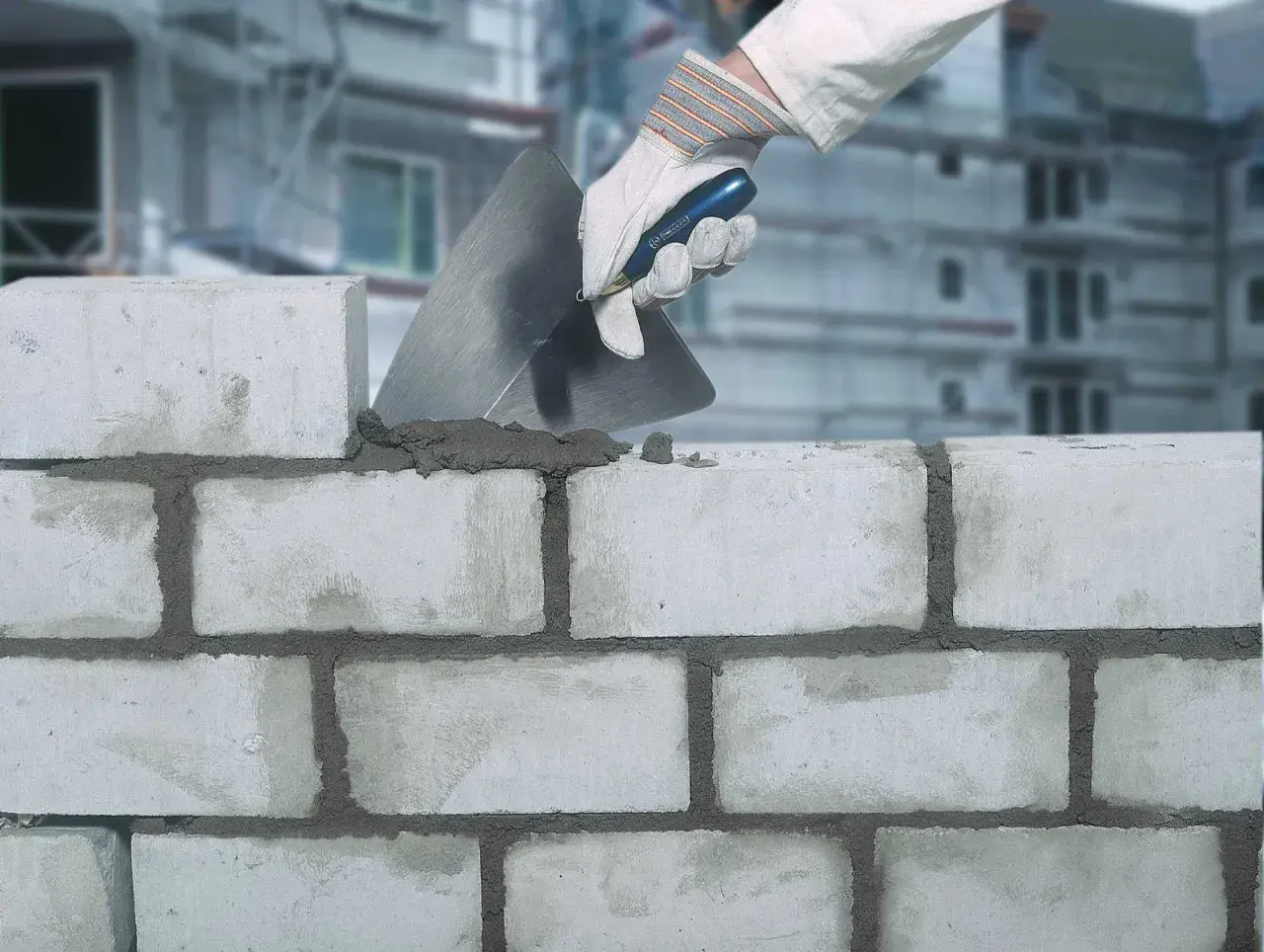 Maurer legt Mörtel mit Kelle auf Ziegelsteine. Der Unterschied zwischen Zement und Beton wird hier beim Mauern deutlich.