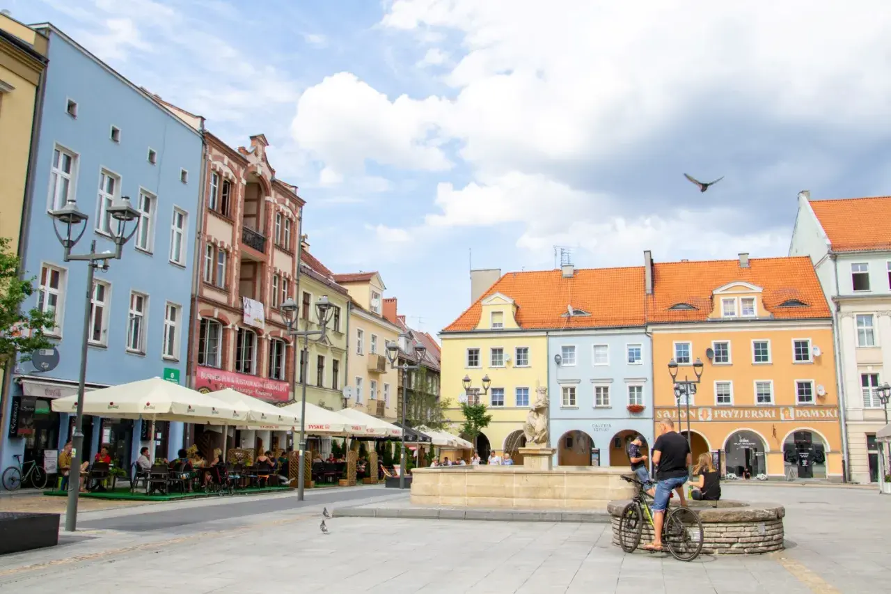 Kolorowy rynek w Gliwicach, idealne miejsce na weekendowe atrakcje. Ludzie siedzą w ogródkach kawiarnianych, a w tle widać zabytkowe kamienice.