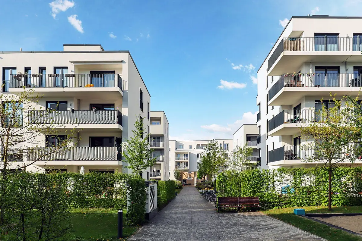 Immeubles modernes avec balcons, chemin pavé, verdure. Une location avec promesse de vente, un lieu de vie prometteur.